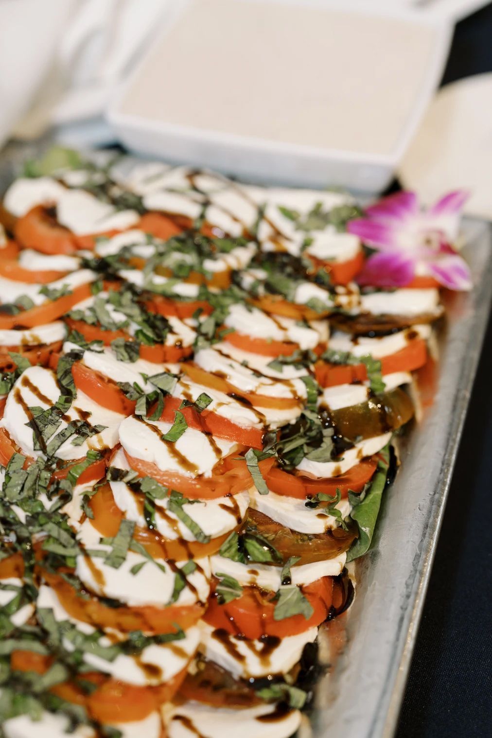 Caprese salad with tomatoes, mozzarella, basil, and balsamic glaze on a platter, sauce in a dish.