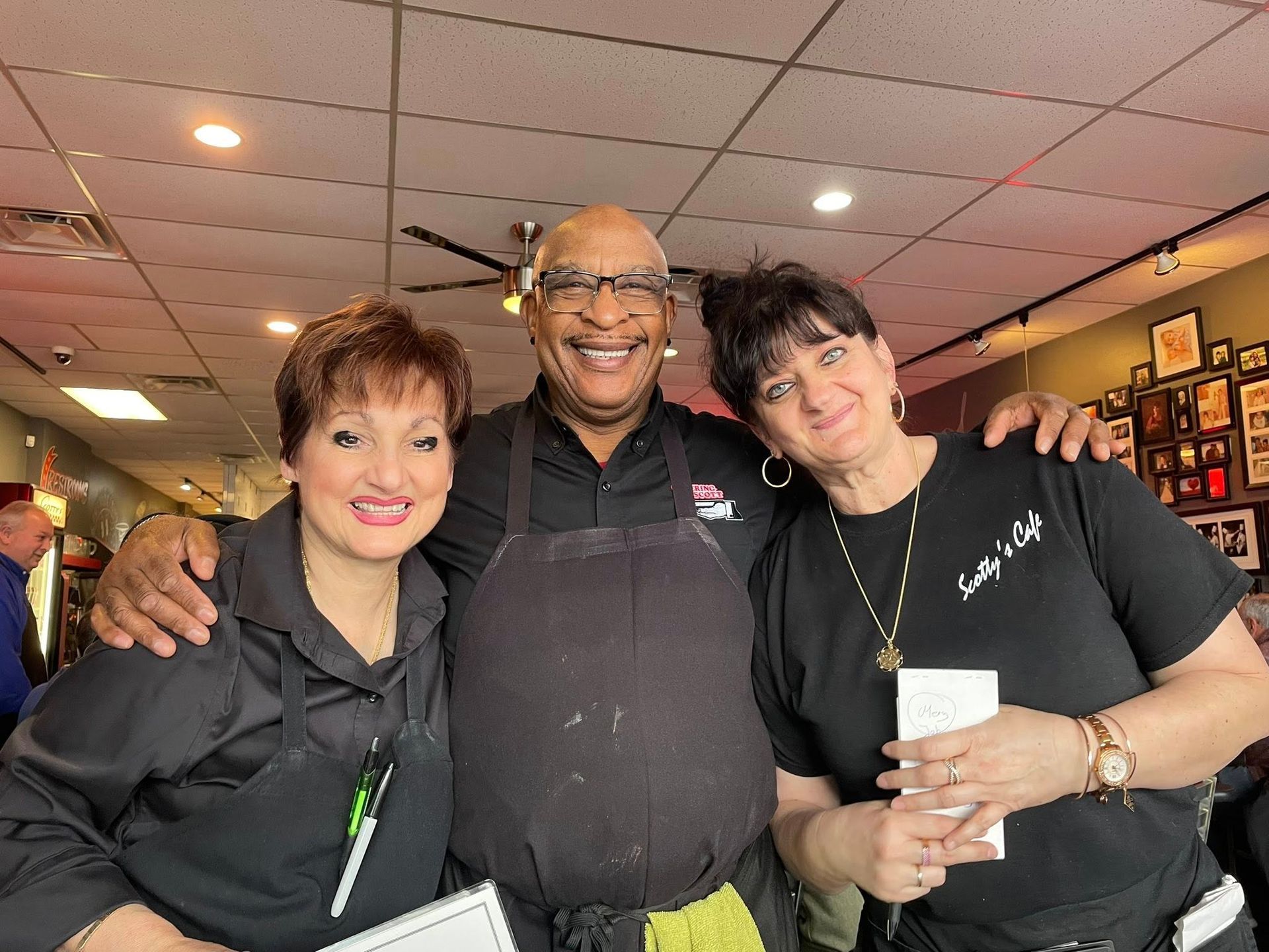 Three people smiling together inside a restaurant. Man in center has arms around two women.