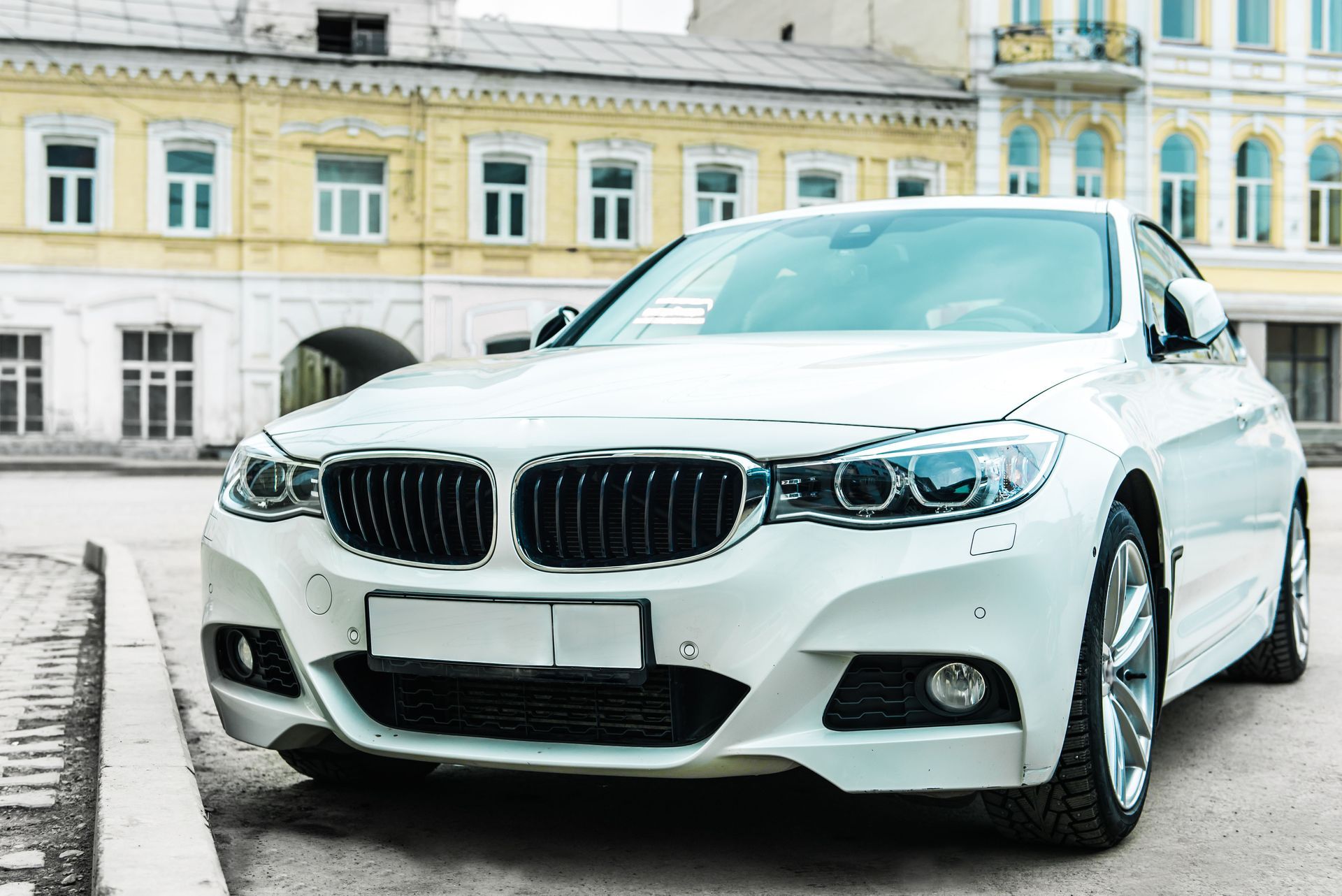 White BMW sedan parked on a city street in front of a historic building