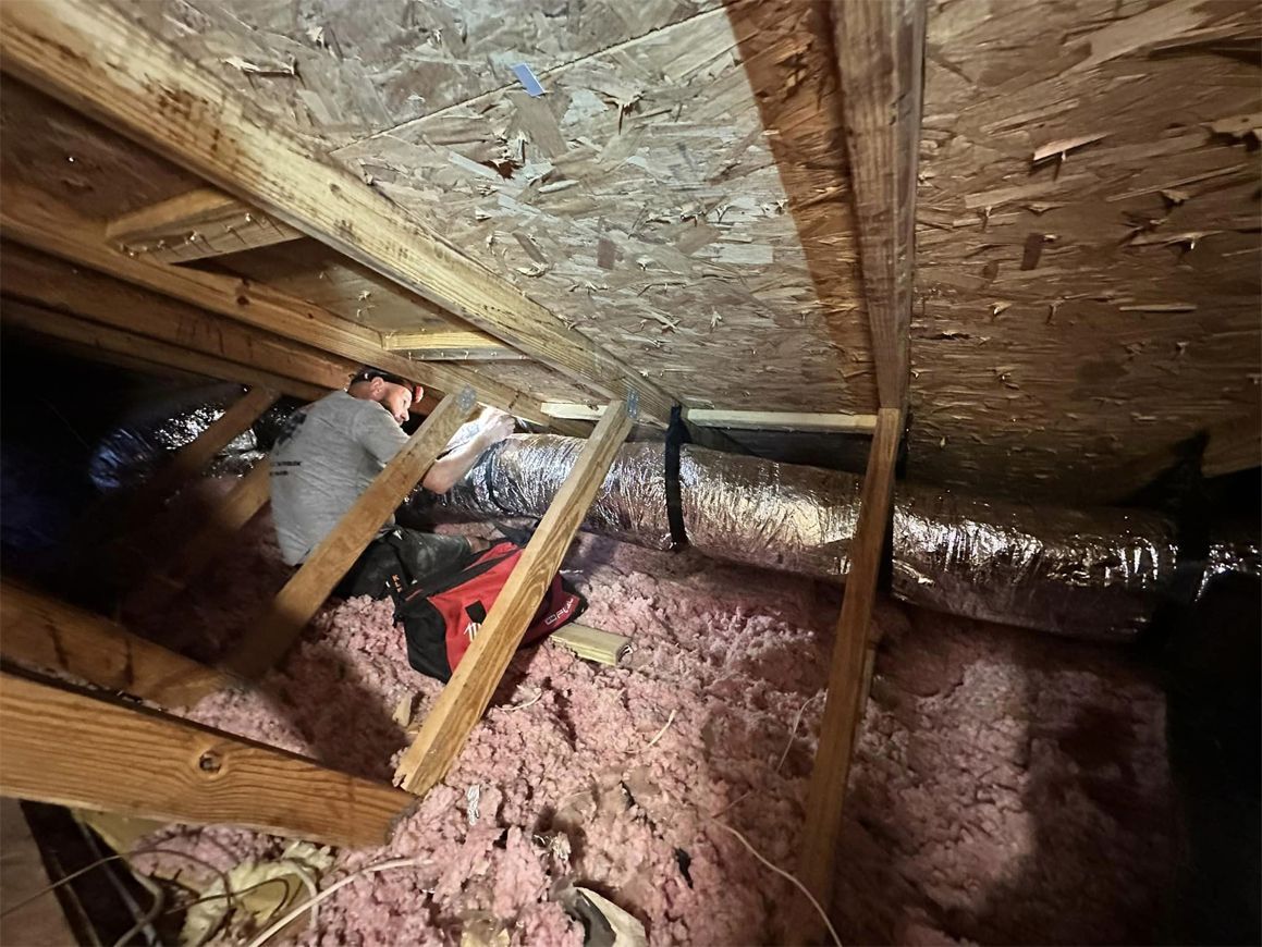A man is working on an air duct in an attic.