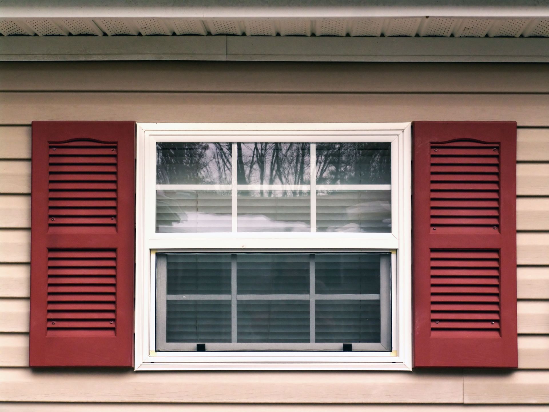 White window with red shutters on a beige house exterior