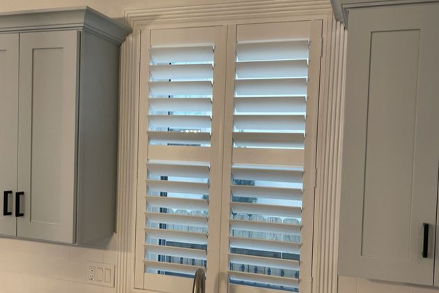 Kitchen window with white plantation shutters flanked by light gray cabinets