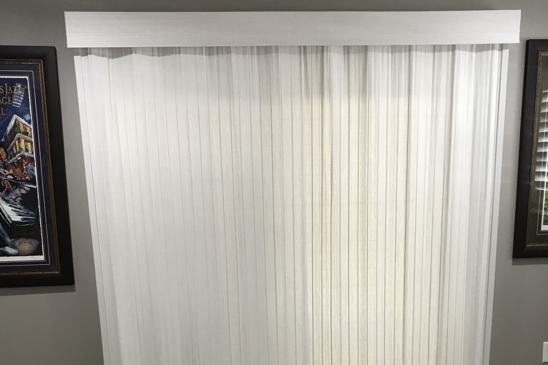 White curtains over a window with framed artwork on both sides.