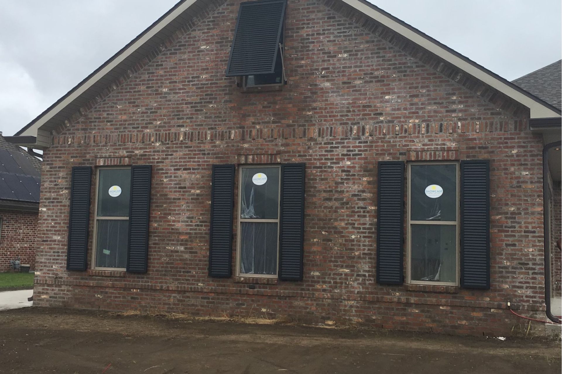 Front view of a small brick house with three windows and dark shutters under a peaked roof.