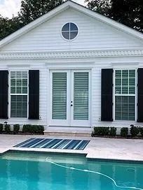 White house exterior with black shutters and a turquoise pool in front