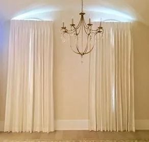 Elegant chandelier centered between cream curtains in a softly lit room