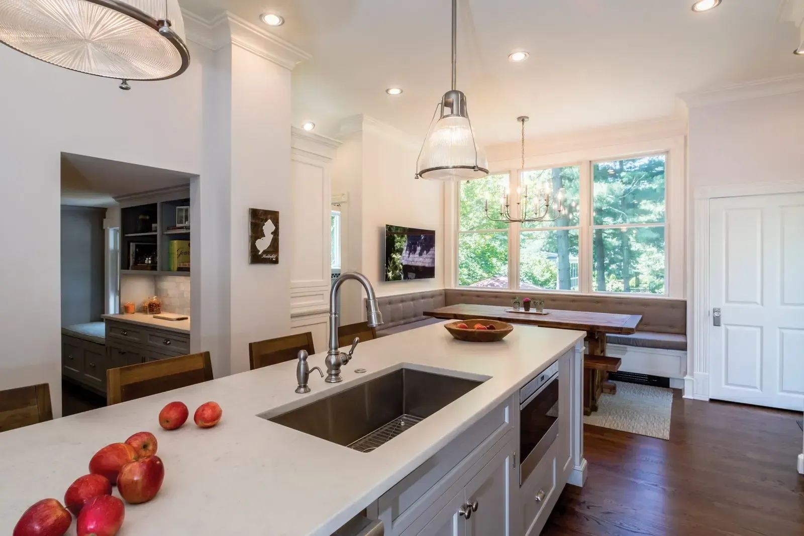 A kitchen with a sink and a bowl of apples on the counter.