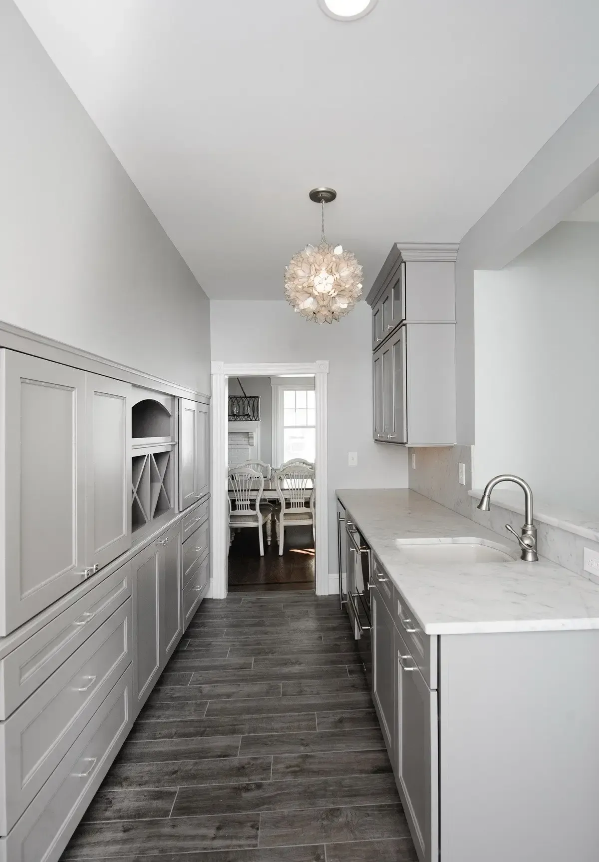 A kitchen with a long hallway leading to a dining room and a sink.
