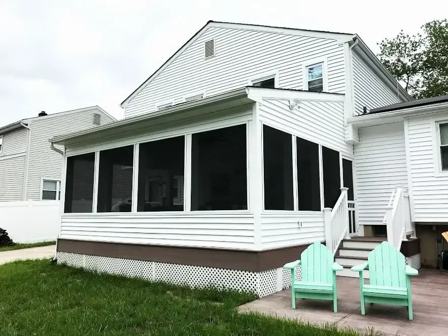 A white house with a screened in porch and two green chairs.