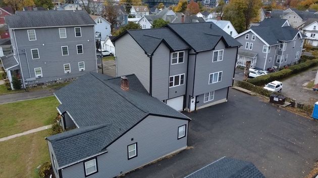 Aerial view of gray apartment buildings with dark roofs and a parking lot in a suburban neighborhood.