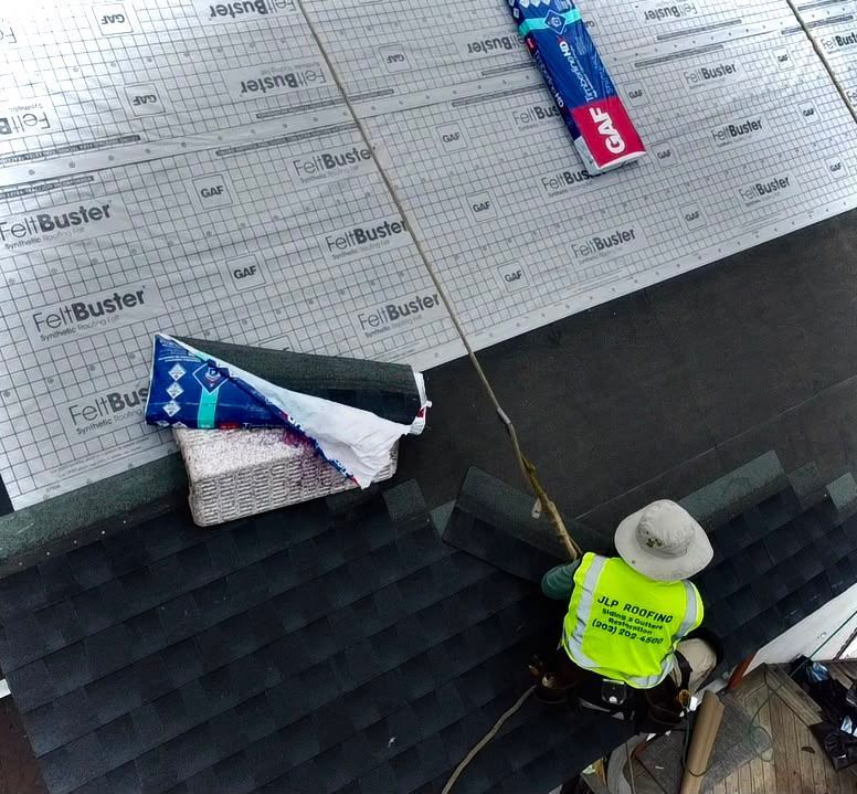Worker on a roof installing a blue-and-red sign beside a paper schedule and tools.