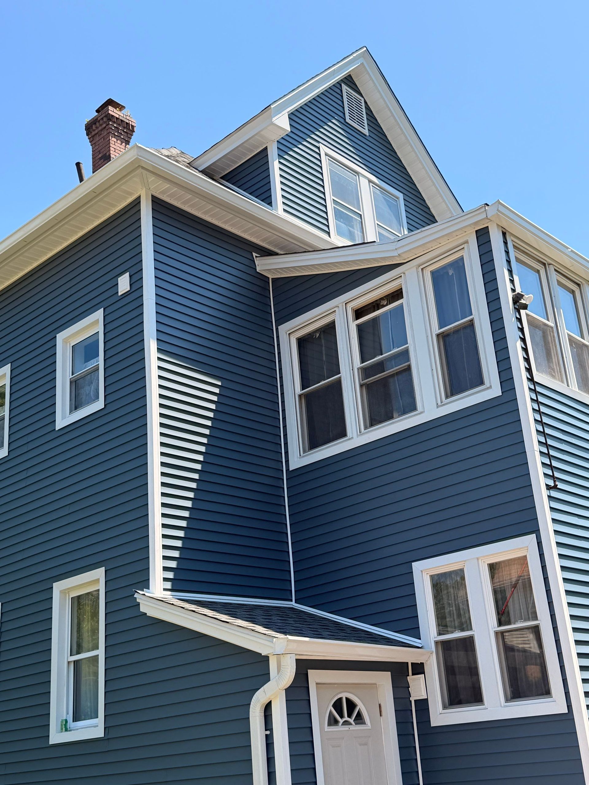 Blue house with white trim and many windows, viewed from below against a clear sky