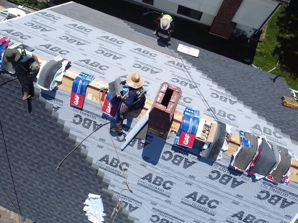 Workers installing roofing shingles on a house roof with ABC logo underlayment visible