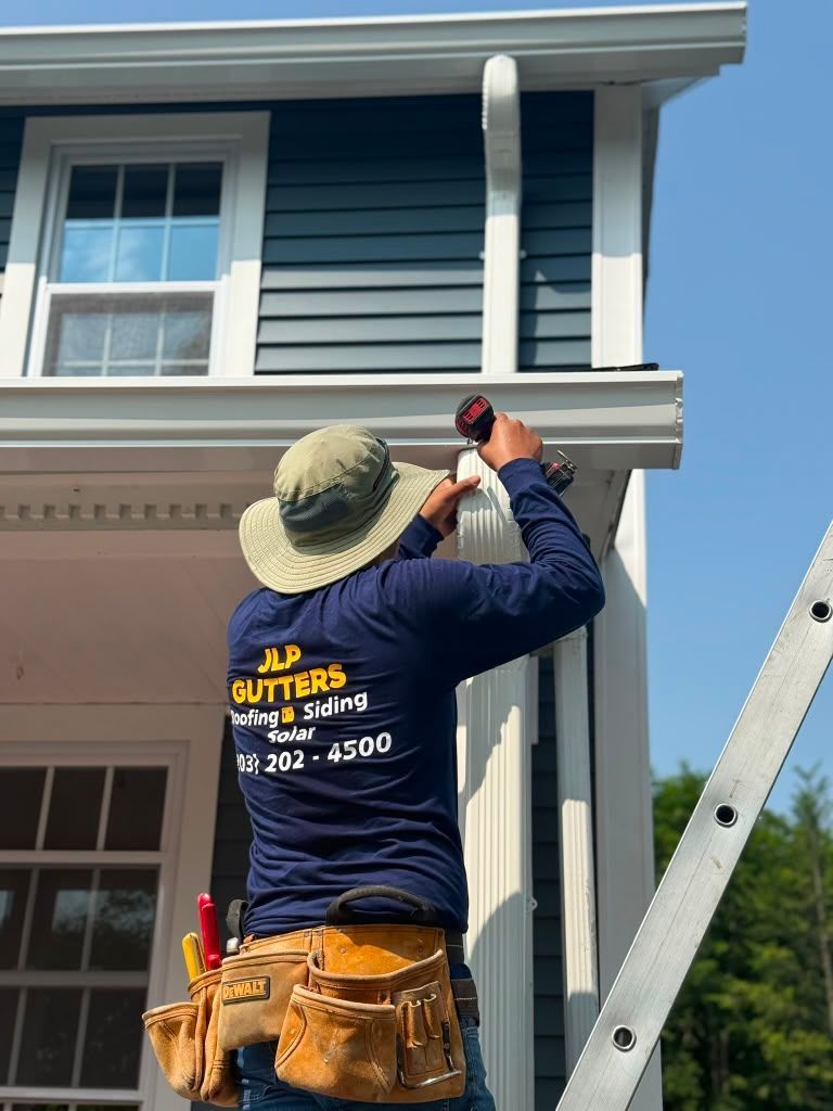 Worker measuring siding on a blue house using a tape measure while standing on a ladder.