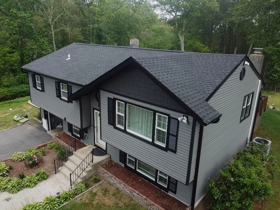 Gray two-story house with black trim and a landscaped front yard on a wooded lot