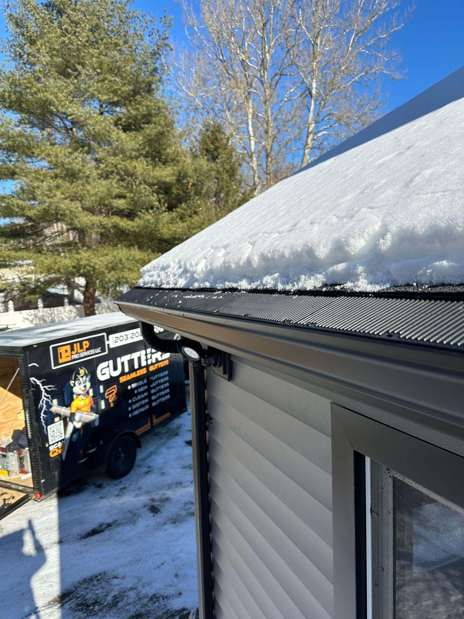 Snow-covered roof edge on a house beside a tree and a truck in a snowy yard