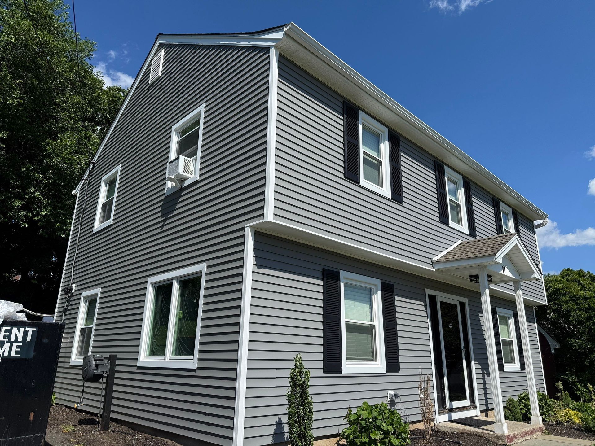 Gray two-story house with white trim and black shutters under a blue sky