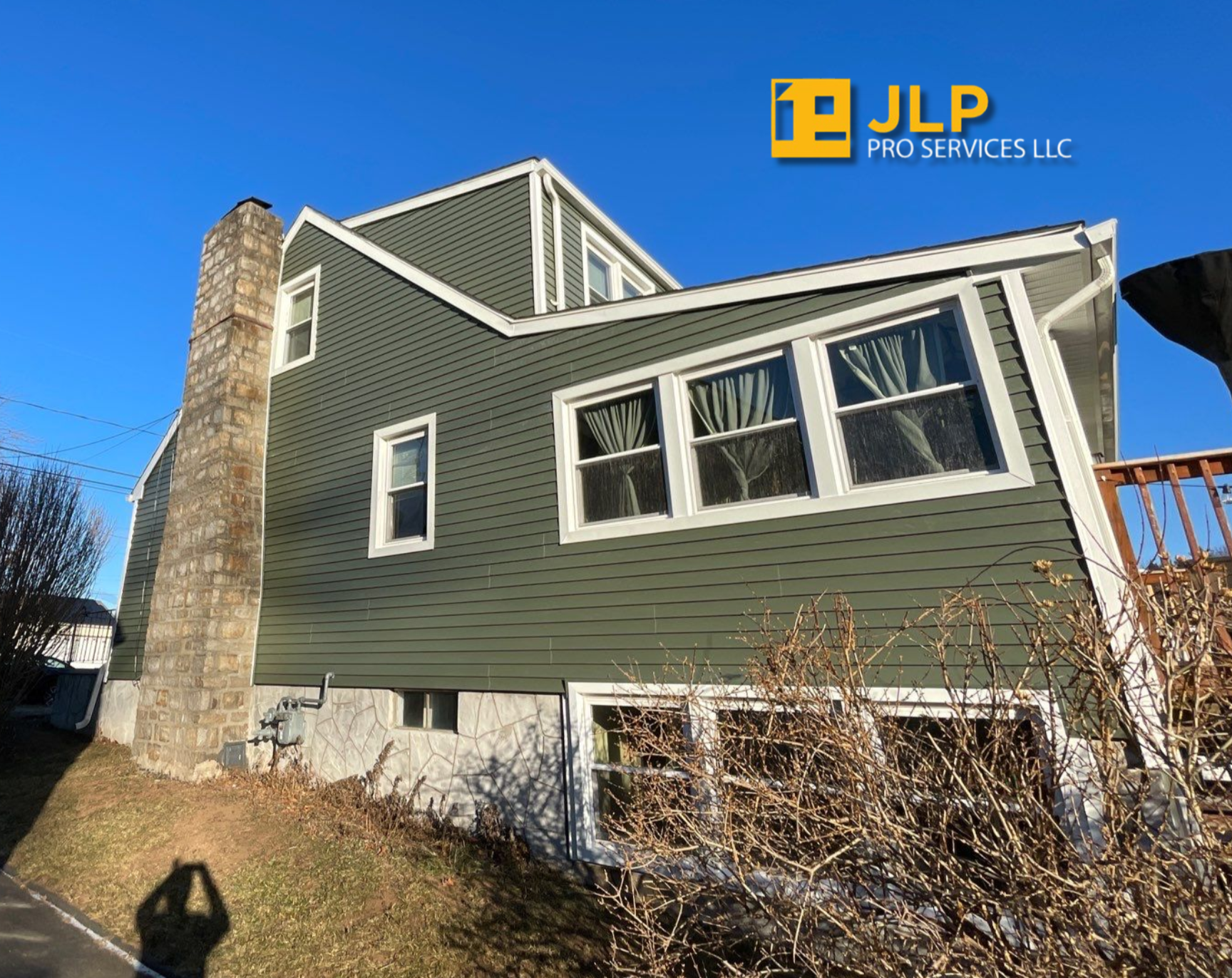 Green house exterior with stone chimney, large windows, and a basement garage under a blue sky