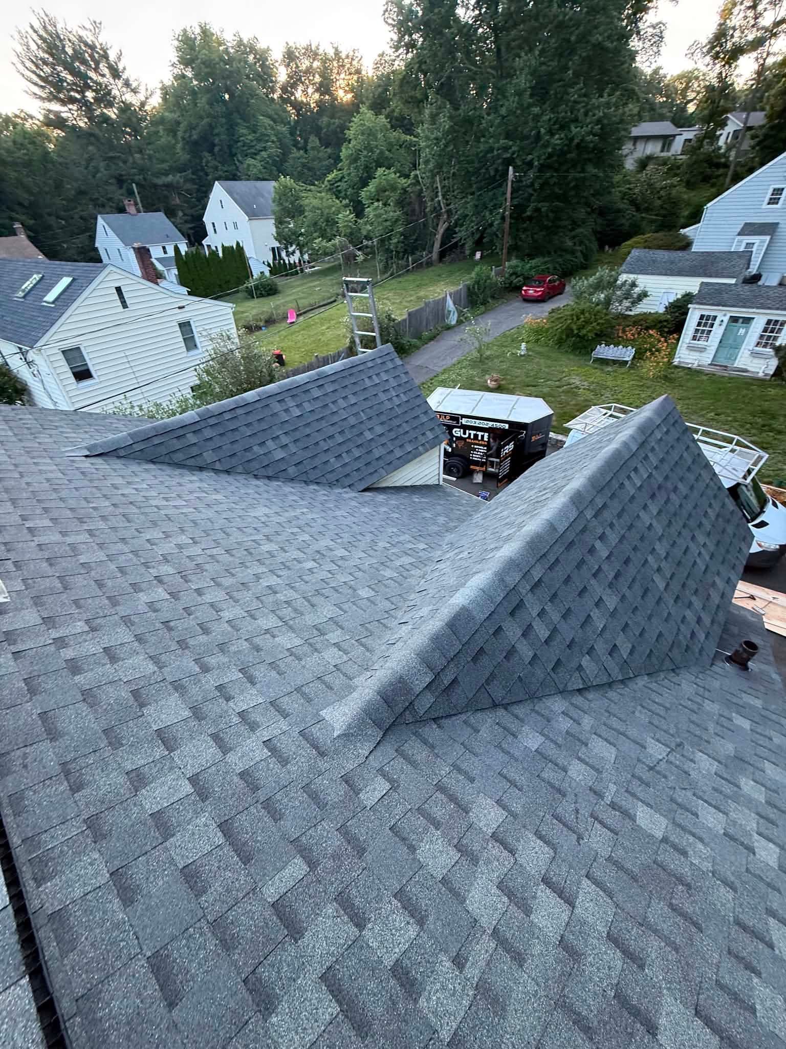 Gray shingled rooftops in a suburban neighborhood at dusk, with trees and houses in the background