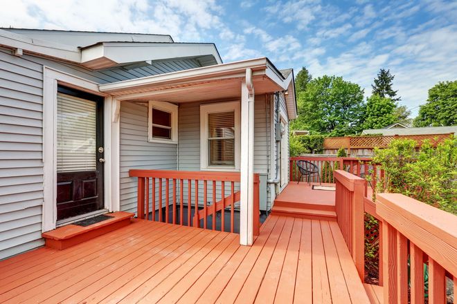 Orange wooden deck with white railing and covered patio beside a house