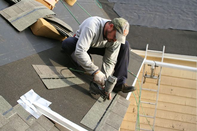 Worker installing roofing shingles on a roof with tools and materials nearby