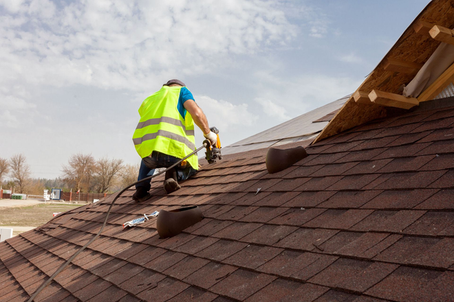 Worker in neon vest cleaning a sloped roof with a power washer
