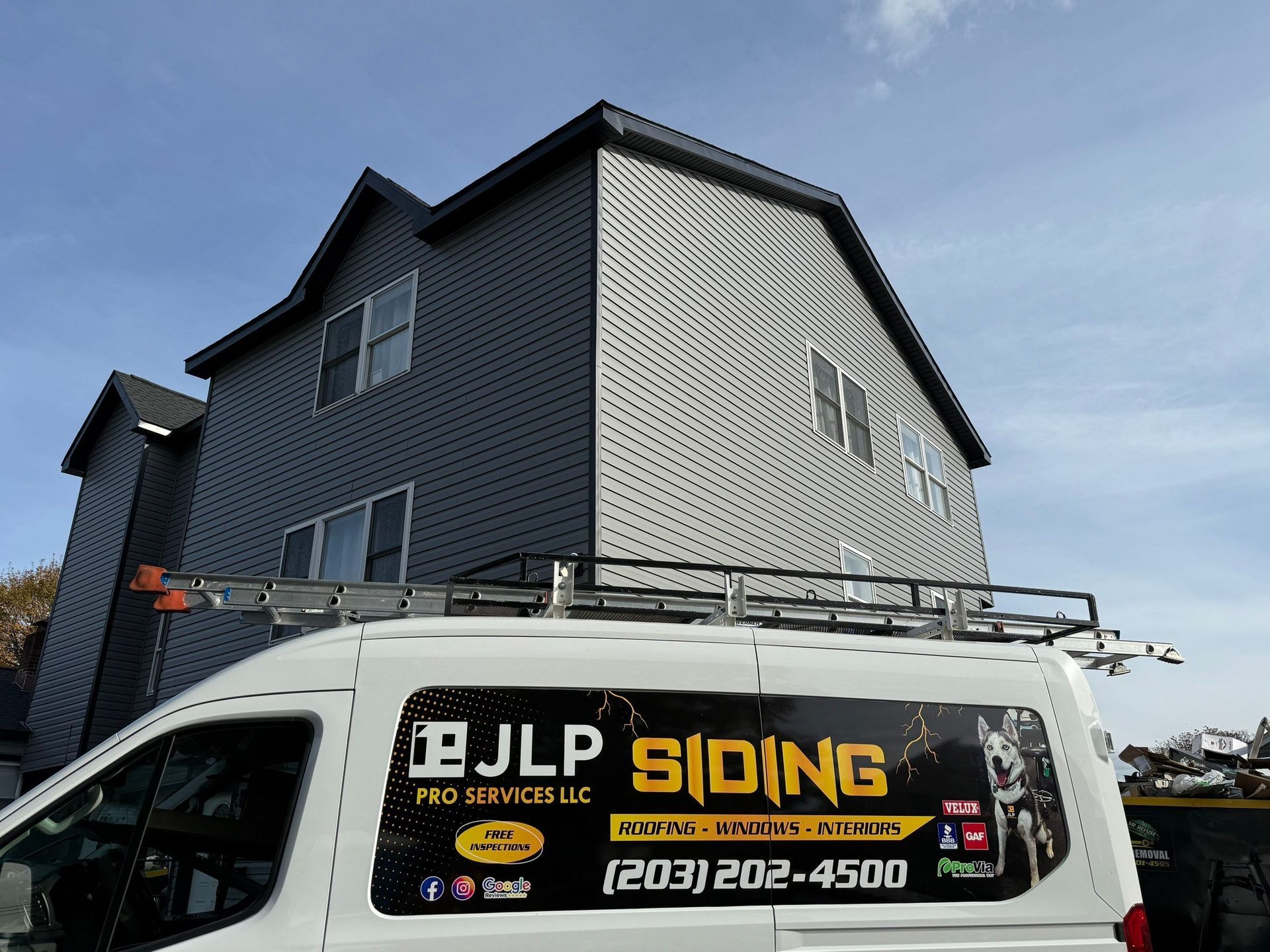 Gray house exterior with a JLP Siding work van parked in front and a ladder on the roof