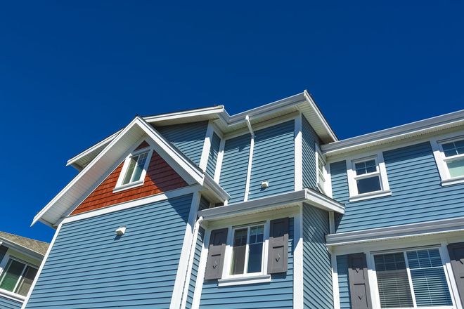 Blue clapboard house exterior with white trim and peaked roofs against a clear blue sky