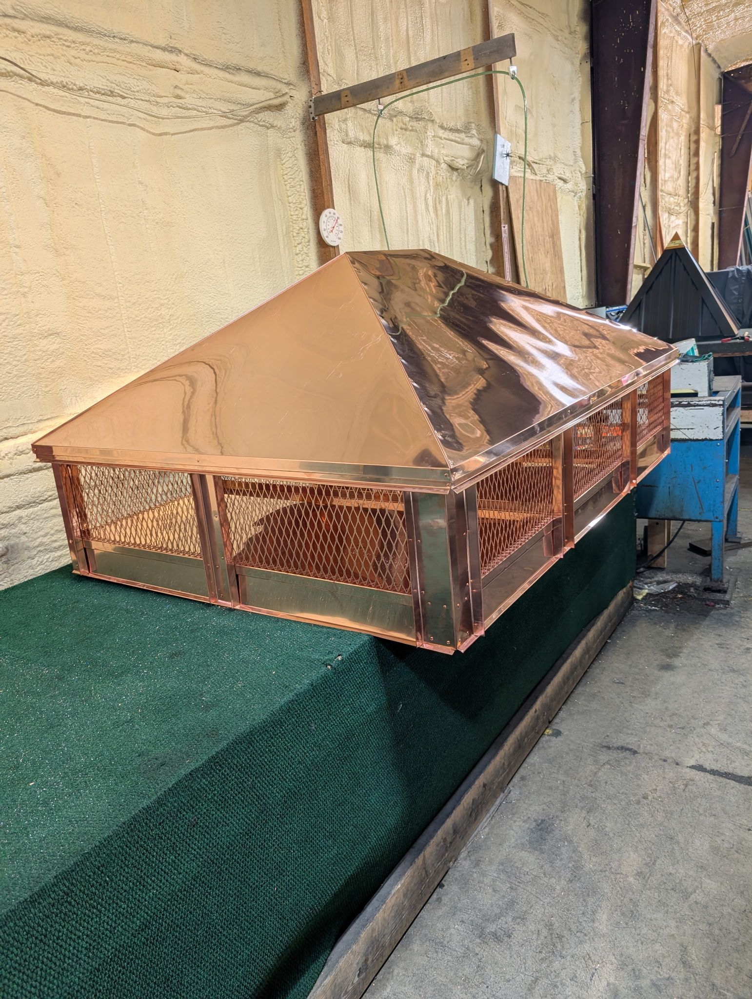 Copper-colored rooftop vent on green mesh platform beside a building wall