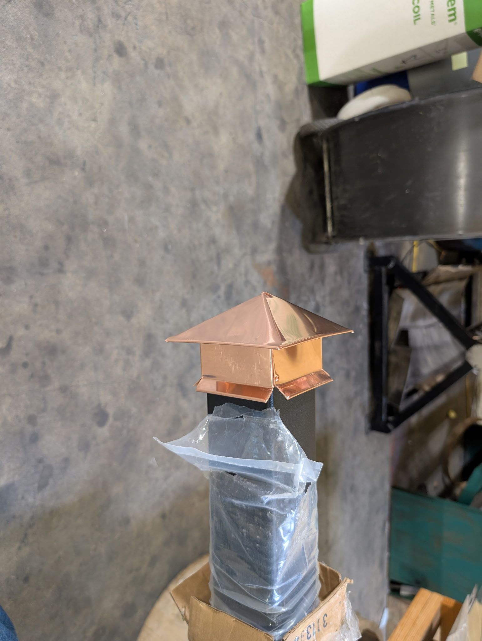 Copper vent cap on a gray wrapped pipe in a workshop/garage setting