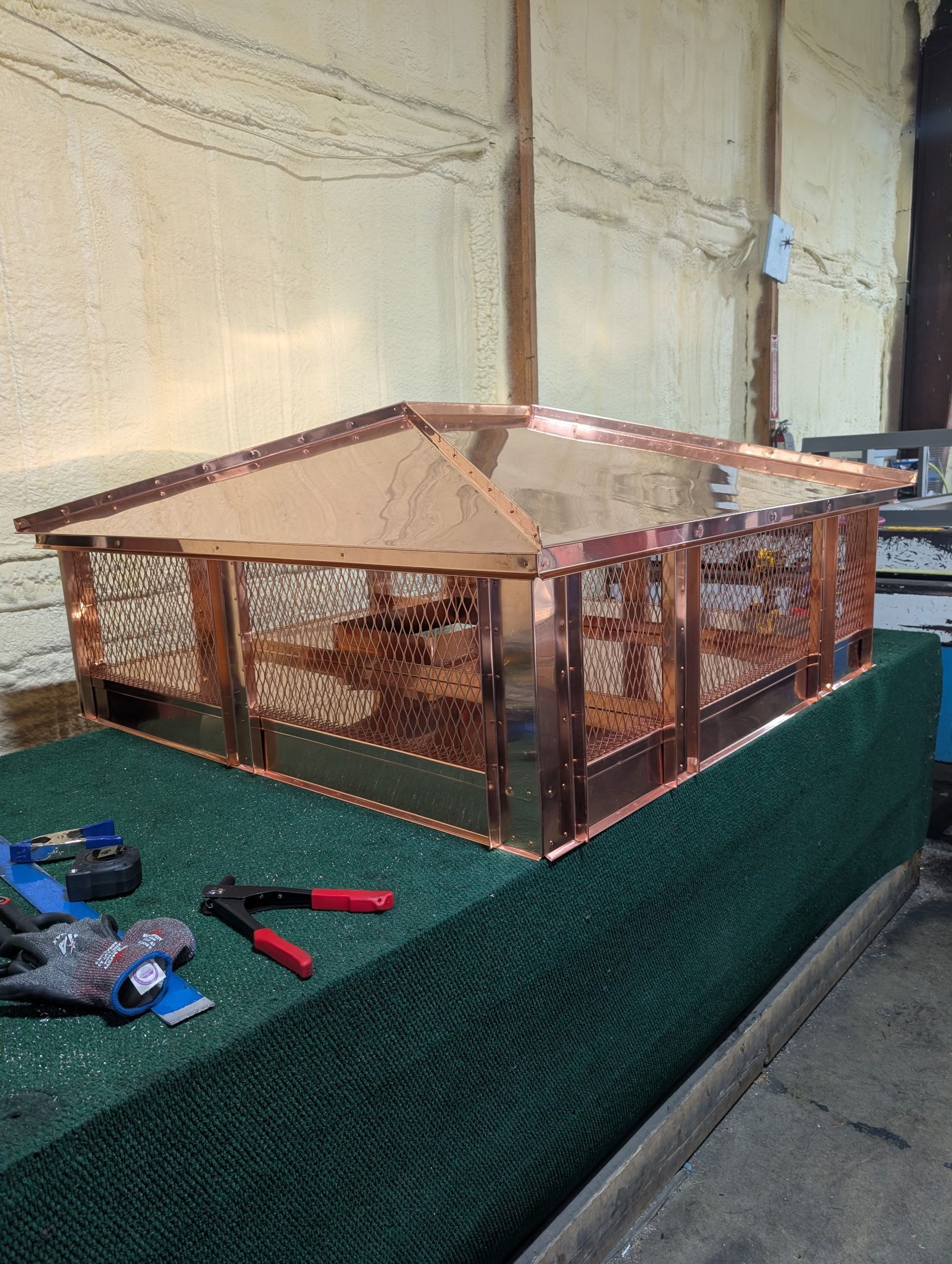 Copper wire animal enclosure on a green workbench with tools nearby