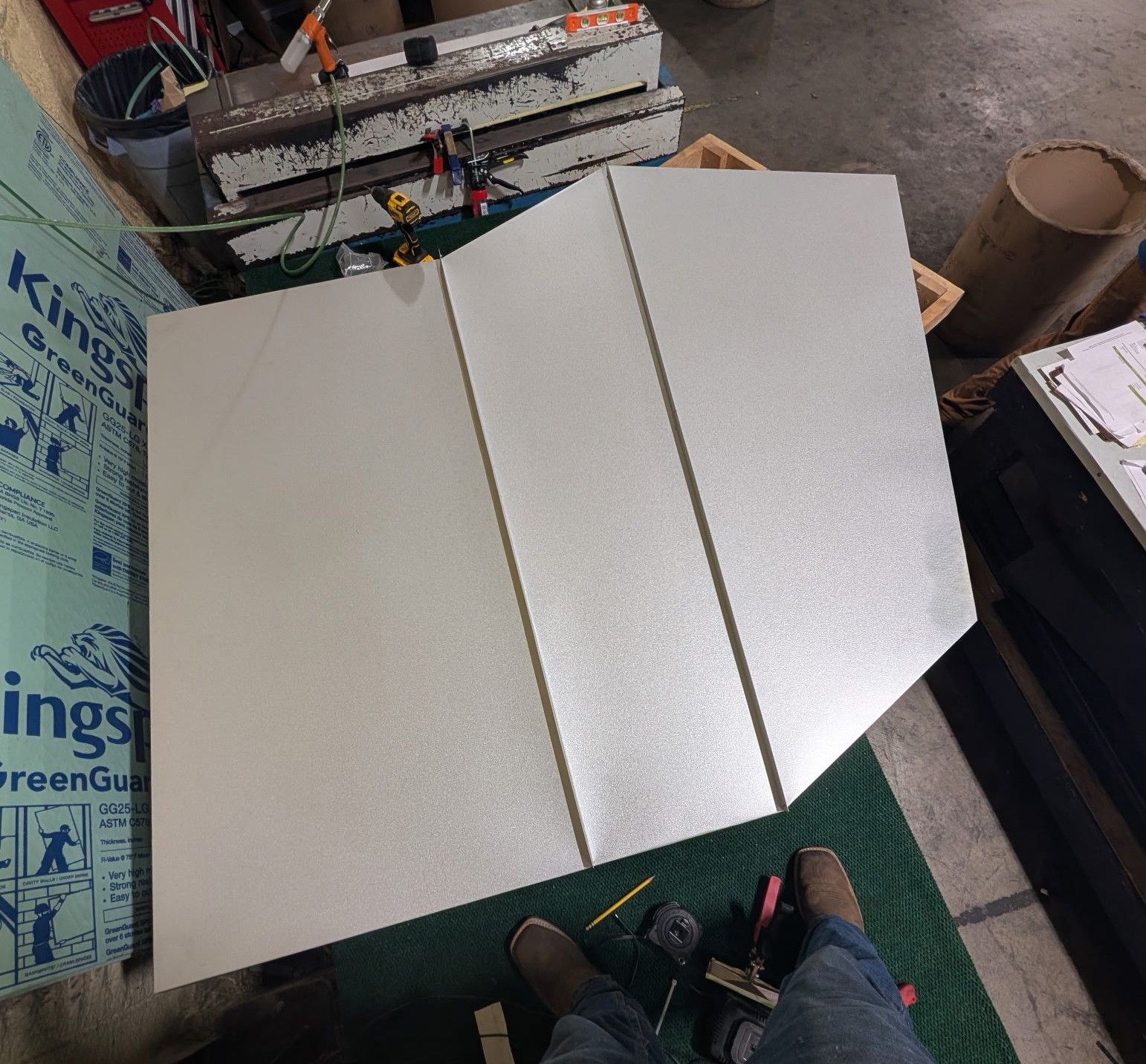 White tri-fold foam board on a workshop floor with tools and materials nearby