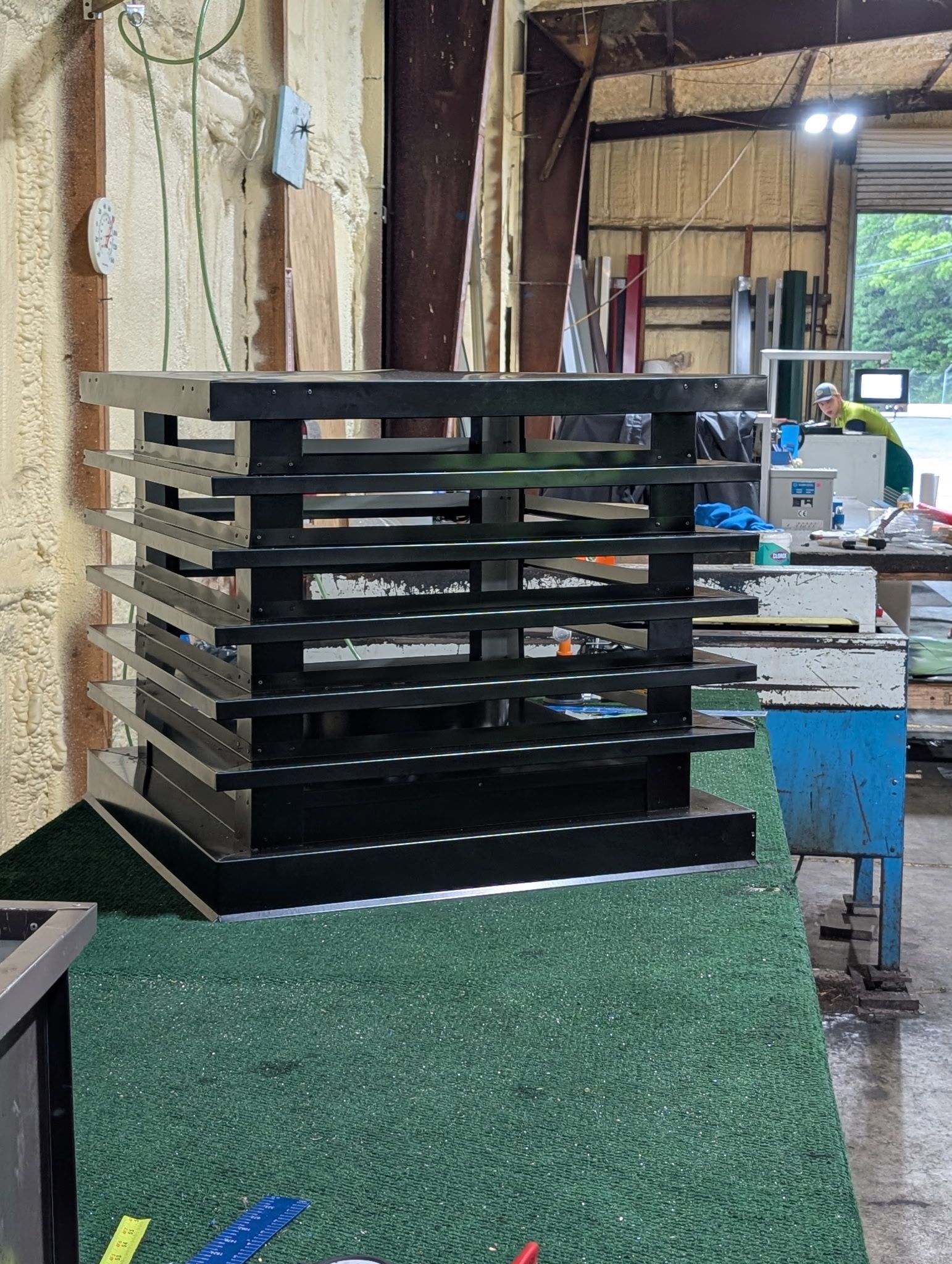 Black metal stack of trays or shelves in an industrial workshop beside a workbench.