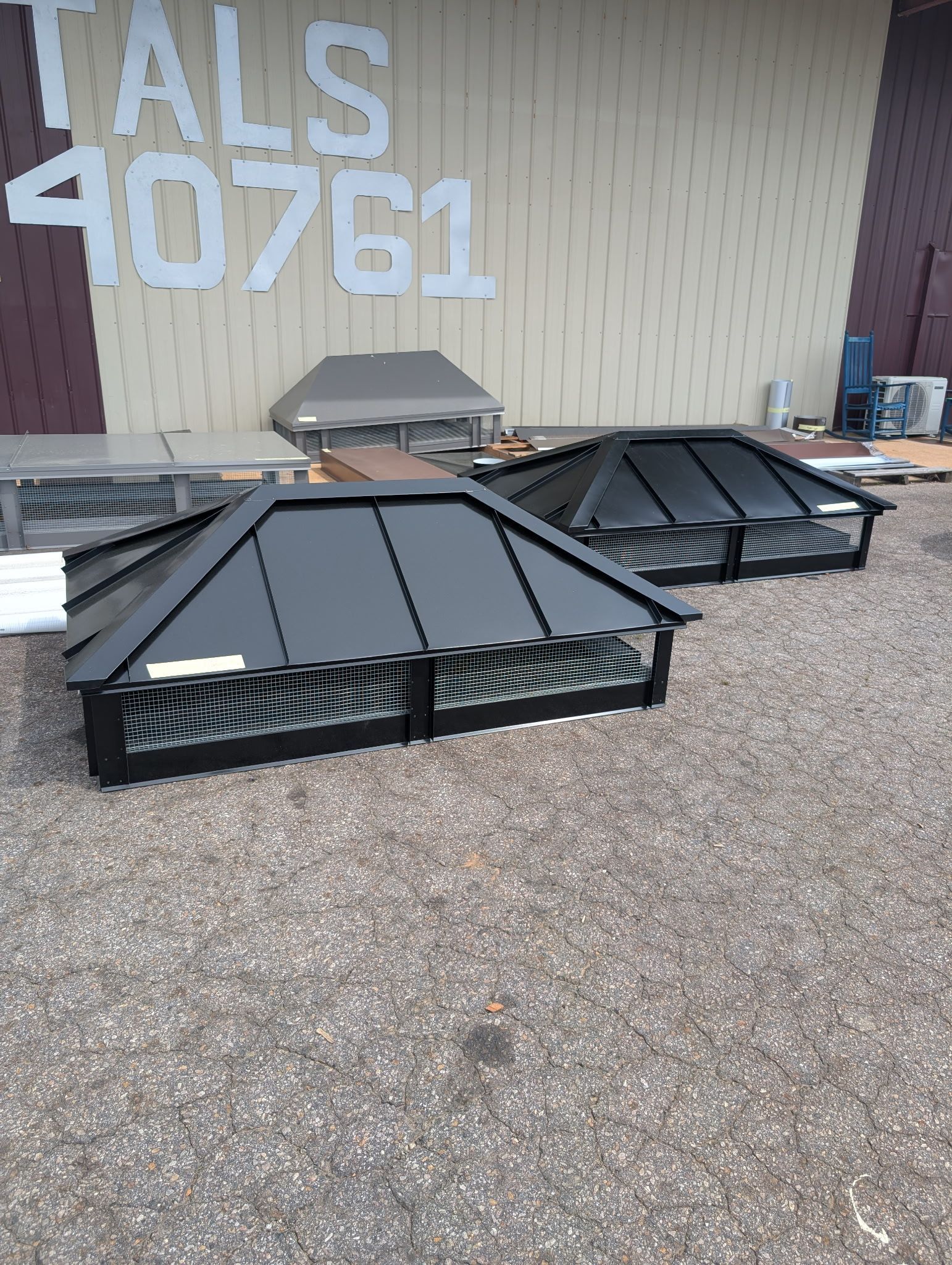 Black metal rooftop equipment stacked on gravel beside a tan building with white numbers painted on the wall