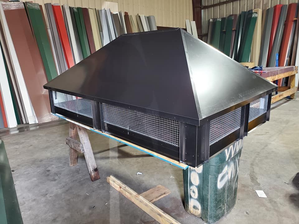 A black chimney cap is sitting on top of a wooden table in a warehouse.