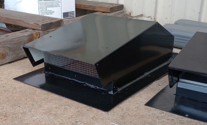 A black metal roof vent is sitting on top of a wooden table.