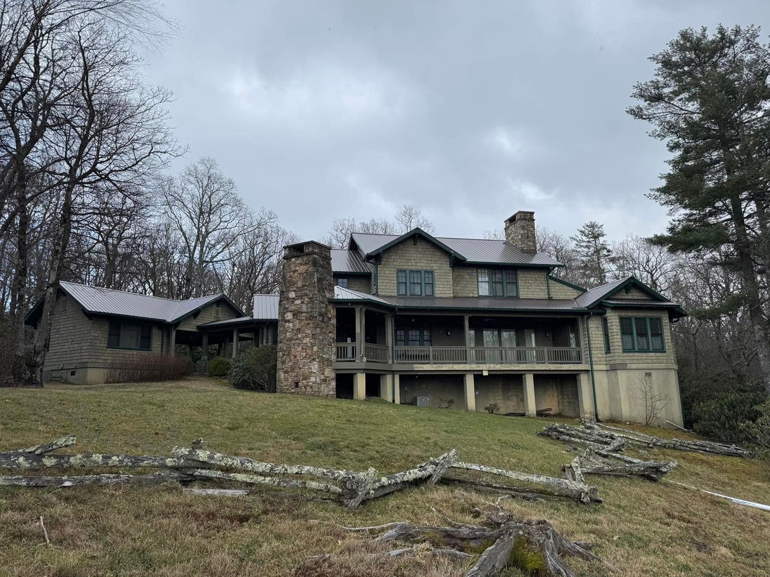 A large house is sitting on top of a grassy hill in the middle of a forest.