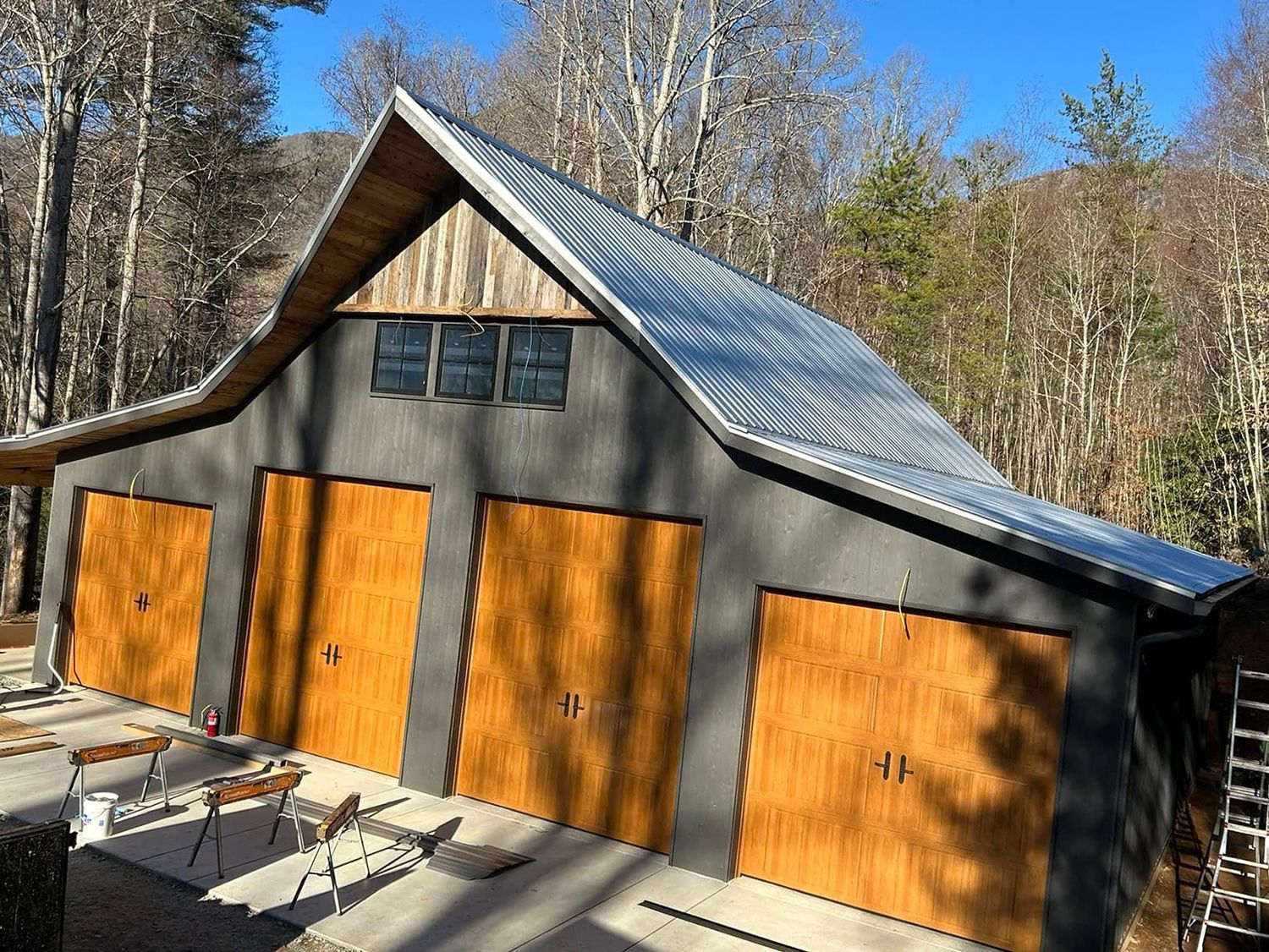 A garage with wooden doors and a metal roof in the middle of a forest.