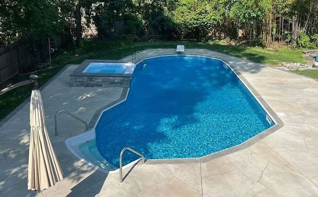 Backyard swimming pool with blue water, concrete deck, and safety fence surrounding it