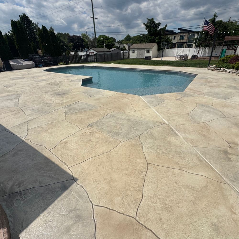Empty backyard swimming pool with tan stamped concrete deck under a cloudy sky