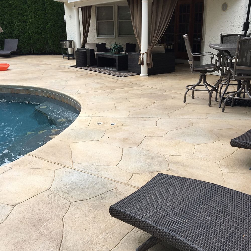 Patio with a curved swimming pool, stone pavers, and wicker lounge furniture under a covered seating area