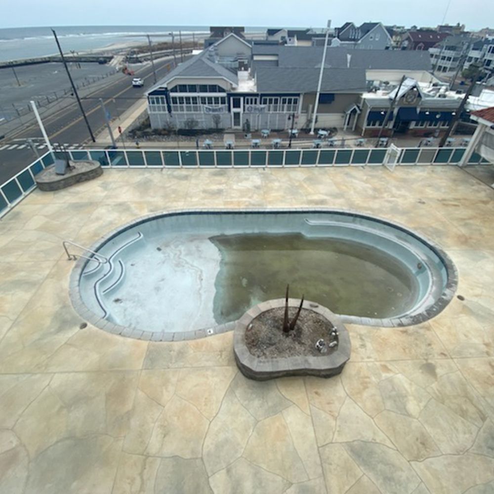 Empty rooftop pool overlooking the beach and boardwalk, with a fire pit in the foreground.