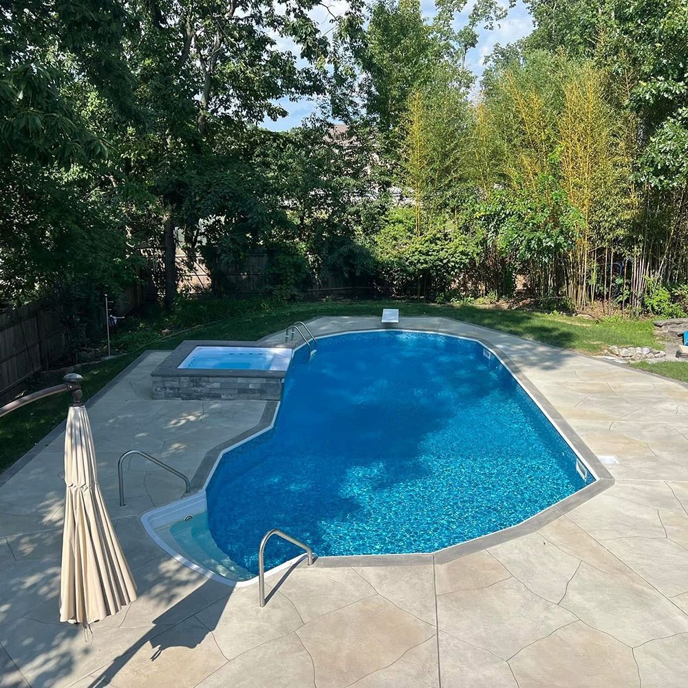 Backyard swimming pool with blue water, surrounding patio, and trees in the background