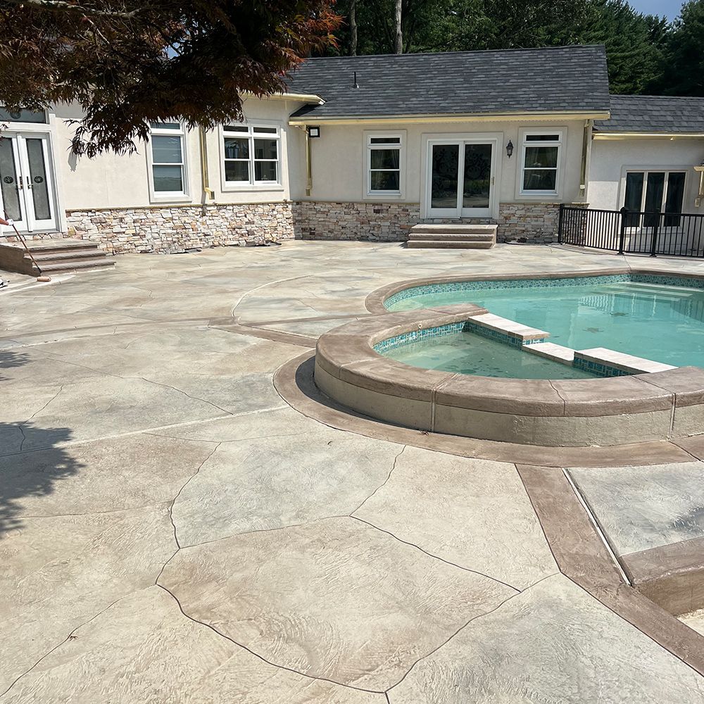 Backyard patio with a curved stone pool and a beige house in the background