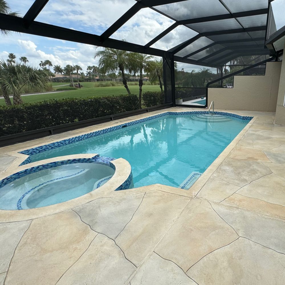 Covered backyard pool with attached hot tub, tan stone deck, and golf course view beyond the screen enclosure