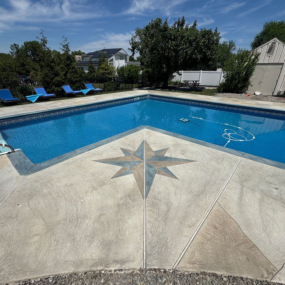 Backyard swimming pool with blue water, lounge chairs, and a compass star design on the concrete deck
