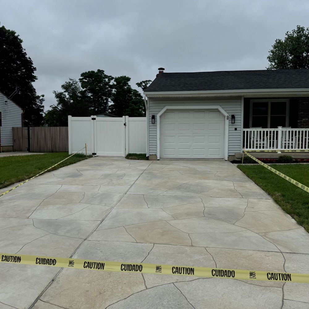 Residential driveway with new concrete, a white garage, and yellow caution tape across the front.