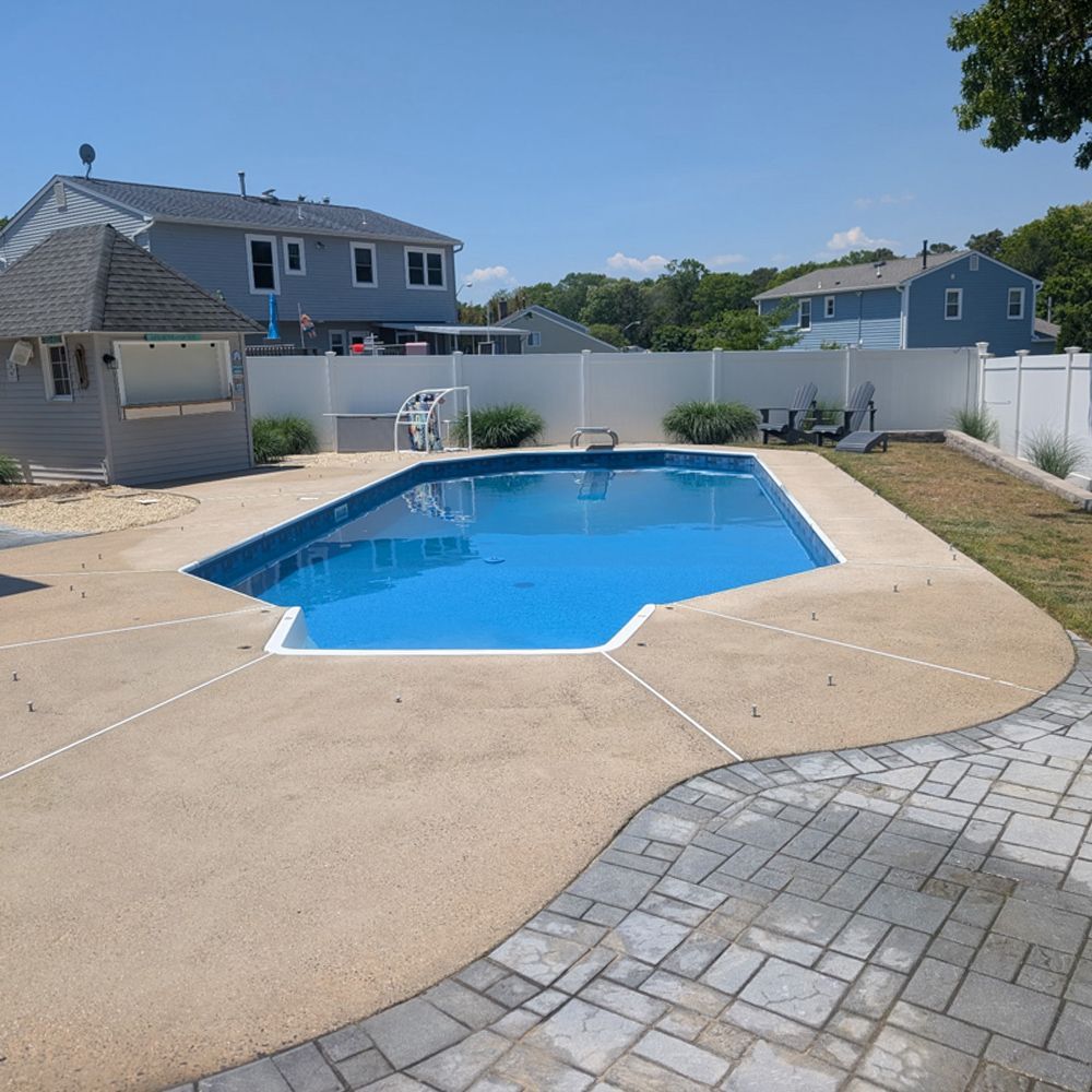 Backyard swimming pool with tan deck and white fence under a clear blue sky