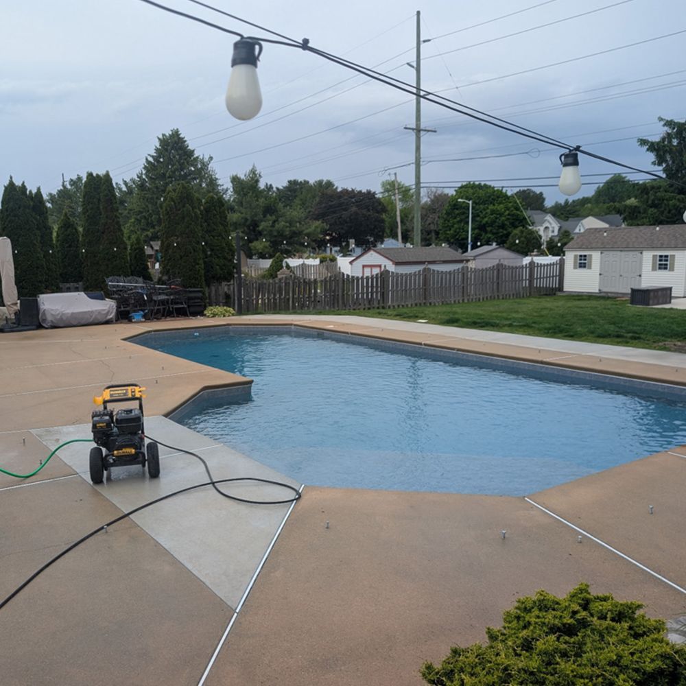 Outdoor pool deck with a pressure washer, string lights, and green lawn under an overcast sky