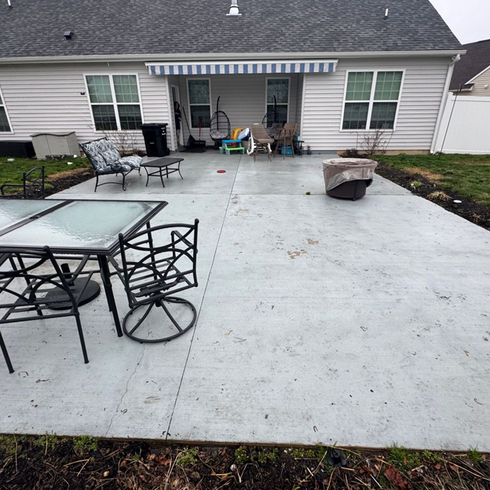 Back patio with concrete slab, outdoor table and chairs, grill, and small seating area under a striped awning.